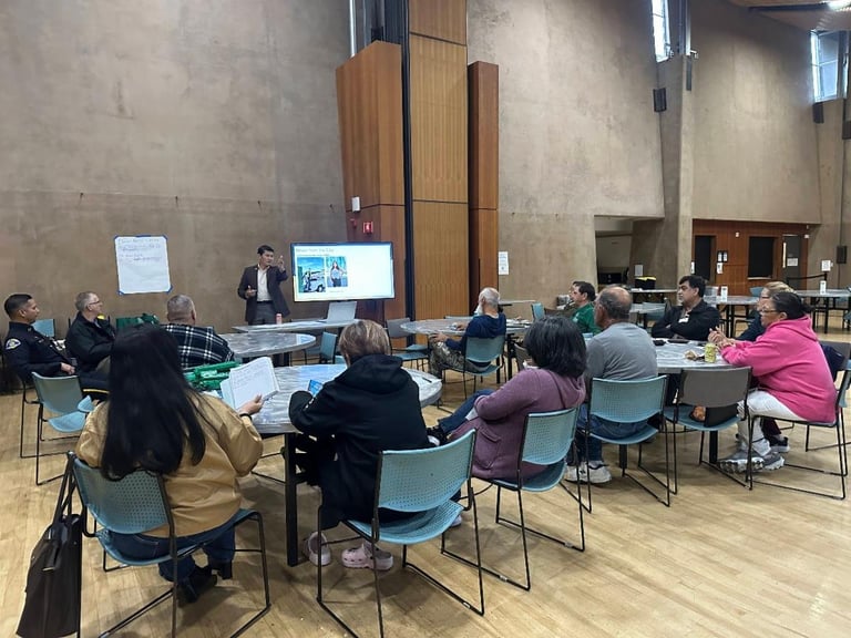 Group of people seated in a circle at a community meeting or presentation in a modern indoor venue with concrete walls.